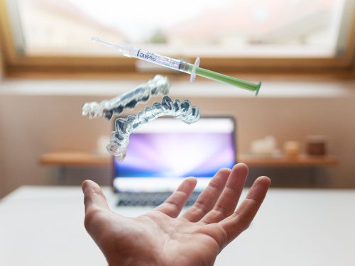 Person's hand tossing a whiteing tray and syringe with whitening gel into the air in front of a tv screen.