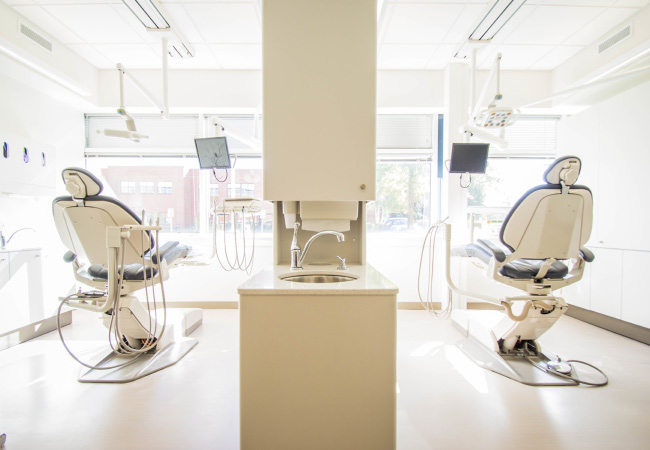 Two dental chairs separated by a large cabinet with a sink in a dental office that has the latest dental technology